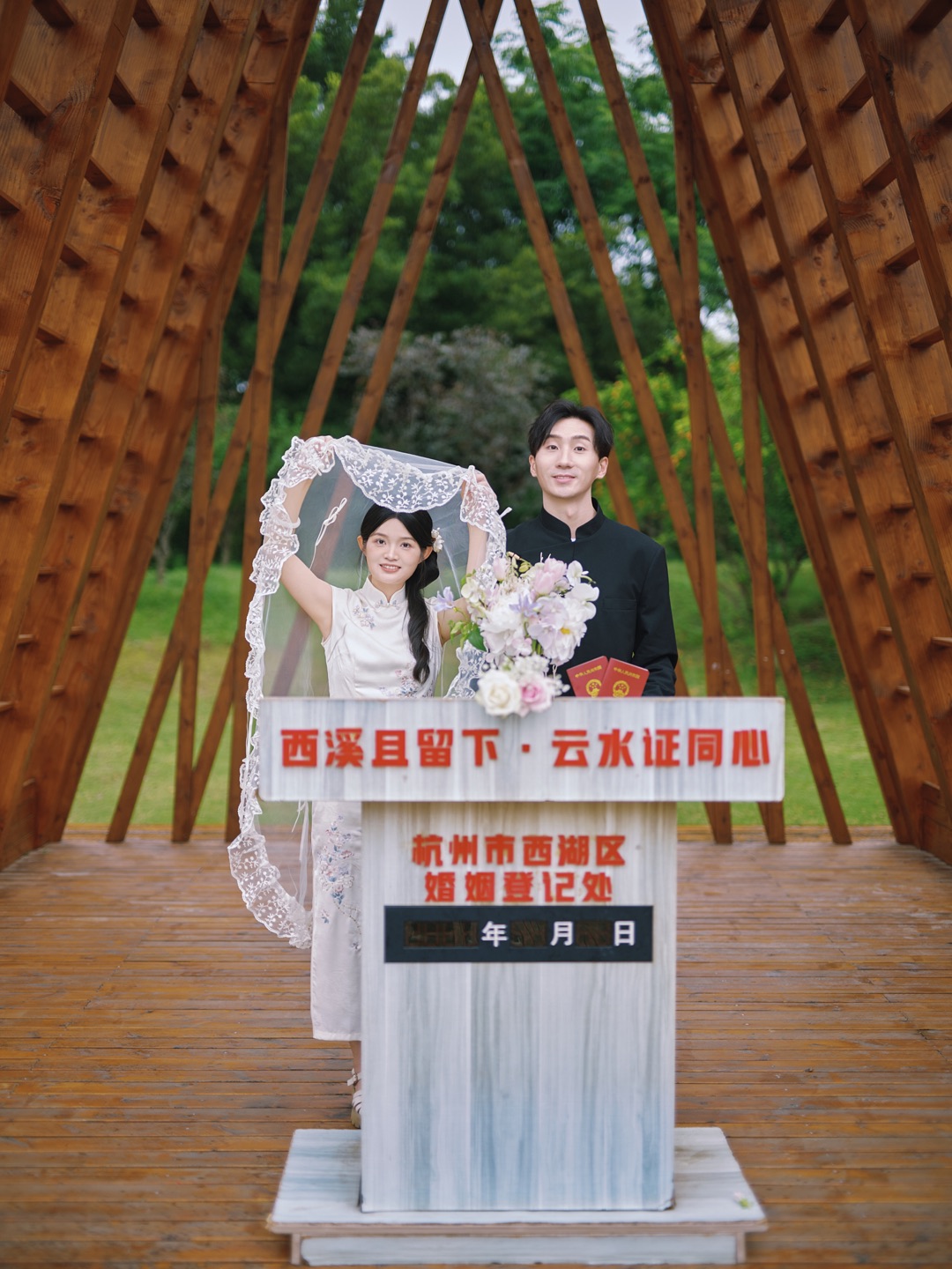 单晶与叶孝璐在木构亭下合影，叶孝璐举起头纱，单晶手持花束与结婚证
